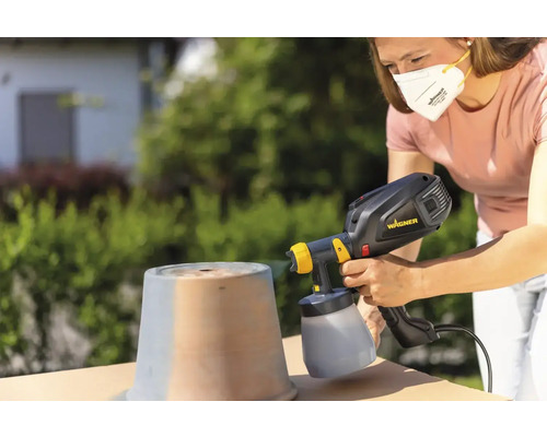 Frau sprüht mit Farbsprühsystem Topf im Freien