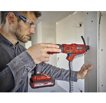 Ein Mann verwendet einen Akku-Trockenbauschrauber von Einhell, um eine Gipskartonplatte zu befestigen. Er trägt dabei eine Schutzbrille und Ohrstöpsel.