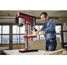 Ein Mann bohrt mit einer Tischbohrmaschine ein Holzbrett.