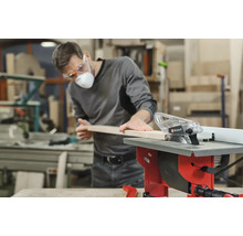 Ein Mann schneidet ein Holzbrett mit einer Einhell Tischkreissäge in einer Werkstatt.