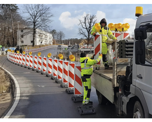 Bauarbeiter stellen eine rot-weisse Verkehrsleiteinrichtung mit Warnleuchten auf einer Straße auf