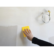 Hand mit gelbem Werkzeug zum Glätten einer Wand.