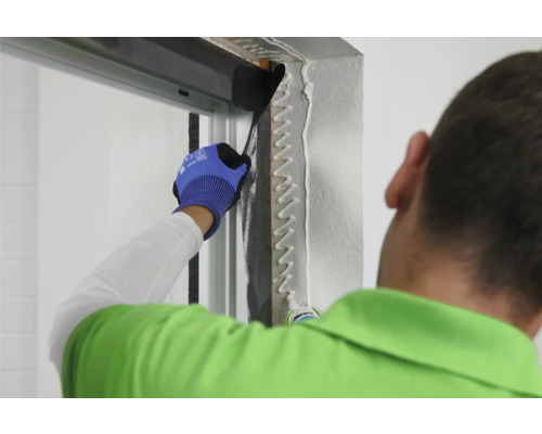 Eine Person trägt Dichtmasse an einem Türrahmen auf, um eine luftdichte Abdichtung zu gewährleisten.