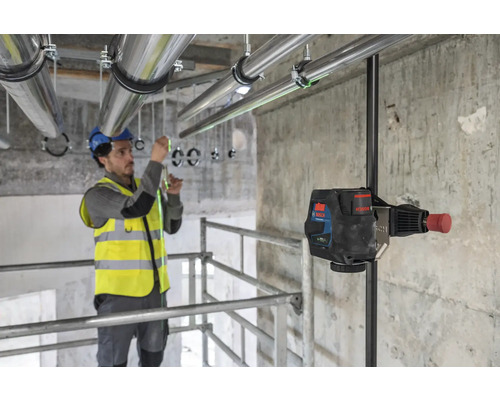 Ein Handwerker arbeitet mit einem Linienlaser, um Rohrleitungen an einer Decke zu installieren.