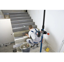 Handwerker verlegt Fliesen auf einer Treppe mit Hilfe eines Linienlasers