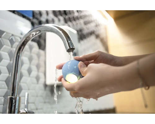 Szene einer Person, die unter einem Wasserhahn einen leuchtenden, runden Gegenstand hält