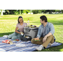 Ein Paar genießt ein Picknick mit einem tragbaren Ninja-Grill, Speisen und Getränken auf einer blau-weiß gestreiften Decke im Freien.