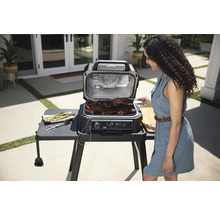 Szene im Freien mit einem Indoor-Grill, auf dem Steaks zubereitet werden, und einer Frau, die mit einer Zange die Steaks wendet