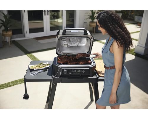 Szene im Freien mit einem Indoor-Grill, auf dem Steaks zubereitet werden, und einer Frau, die mit einer Zange die Steaks wendet