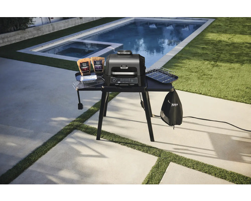 Elektrischer Grill mit Zubehör auf einer Grillstation im Freien.