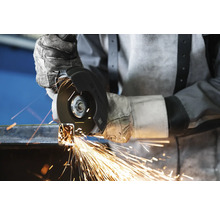 Eine Person trägt Handschuhe und benutzt einen Winkelschleifer zum Schneiden von Metall, wobei Funken entstehen.