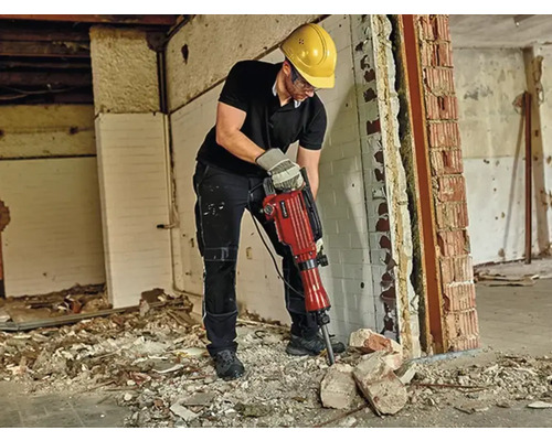 Mann arbeitet mit einem Abbruchhammer auf einer Baustelle, Schutzhelm und Schutzbrille werden getragen.