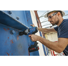Ein Mann mit Schutzhelm verwendet einen Akku-Schlagschrauber an einer blauen Stahlkonstruktion.