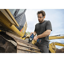 Ein Mann mit Schutzbrille arbeitet mit einem Akku-Schlagschrauber an einer Baumaschine.