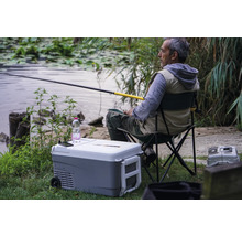 Angler sitzt mit Angel neben einer Kühlbox am See