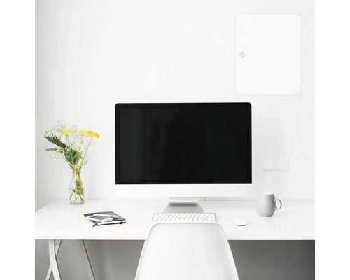 Schreibtisch mit Computer, Tastatur, Maus, Tasse, Blumen und Zubehör in einem hellen Raum.