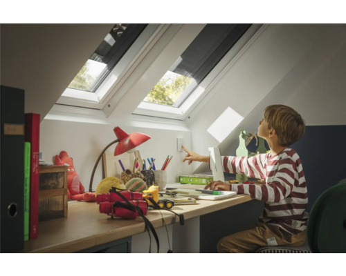 Junge an einem Schreibtisch unter einem Dachfenster mit Verdunkelungsrollo