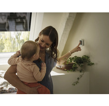 Frau mit Baby bedient Smart Home Steuerung im Dachgeschoss
