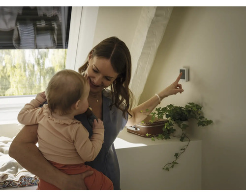 Frau mit Baby bedient Smart Home Steuerung im Dachgeschoss