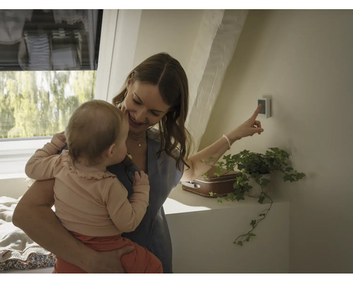 Frau mit Kind, die auf ein Smart Home Gerät an der Wand zeigt