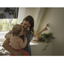 Frau mit Baby bedient Smart Home Steuerung an der Wand
