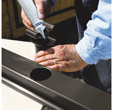 Person trägt Dichtstoff auf ein Fallrohr für die Regenrinne auf