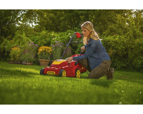 Frau bedient einen Rasenmäher im Garten.