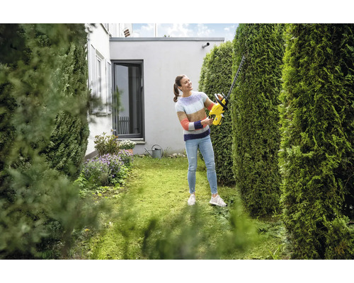 Frau schneidet Hecke mit einer Heckenschere im Garten.