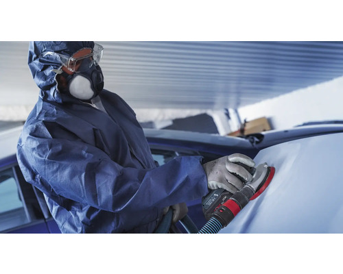 Eine Person in Schutzkleidung schleift ein Auto mit einem Schleifgerät.