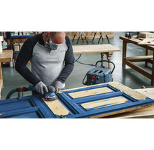 Eine Person schleift eine blaue Holztür mit einem Exzenterschleifer, der an einen Staubsauger angeschlossen ist.