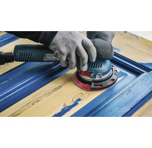 Ein Mann schleift mit einem Exzenterschleifer ein blau gestrichenes Holzbrett