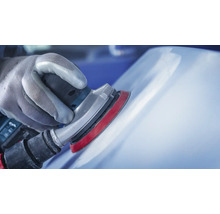 Hand mit Schutzhandschuh schleift mit einem Exzenterschleifer eine Oberfläche.