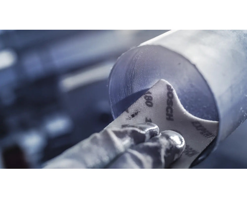 Hand mit Schutzhandschuh schleift ein Rohr mit Schleifpapier der Körnung 180 von Bosch