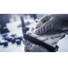 Eine Person mit Handschuhen befestigt Schleifpapier auf einem Handschleifer