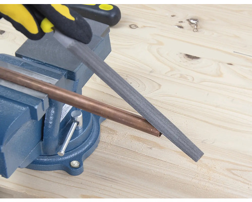 Eine Rohrzange hält ein Kupferrohr, das mit einer Feile bearbeitet wird.