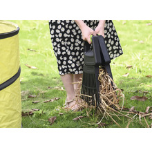 Eine Person benutzt eine Laubaufnahme zum Aufsammeln von Laub auf einer Rasenfläche neben einem Gartensack.