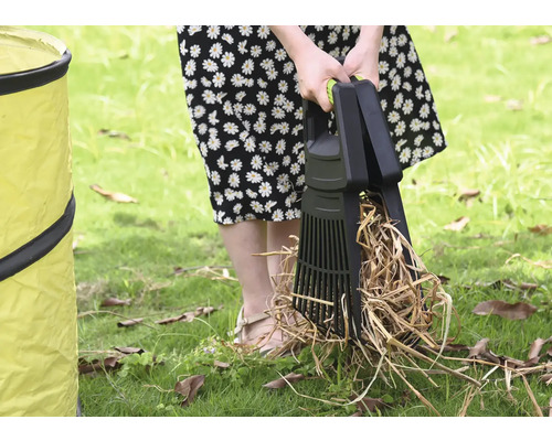 Eine Person benutzt eine Laubaufnahme zum Aufsammeln von Laub auf einer Rasenfläche neben einem Gartensack.