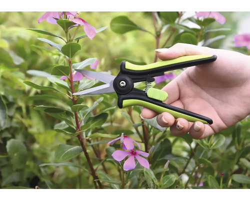 Gartenschere in einer Hand vor Pflanzen