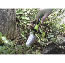 Nahaufnahme einer Hand, die eine kleine Gartenschaufel in Erde neben Pflanzen hält