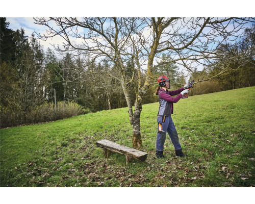 Frau mit Schutzhelm schneidet Baum mit einer Astschere in einem Garten.