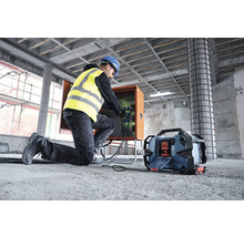 Ein Bauarbeiter mit Schutzhelm und Sicherheitsweste schliesst ein Kabel an eine Stromverteilerbox auf einer Baustelle an