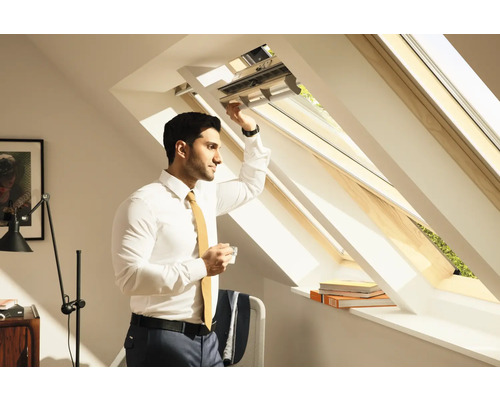 Ein Mann öffnet ein Dachfenster und hält eine Tasse in der Hand.