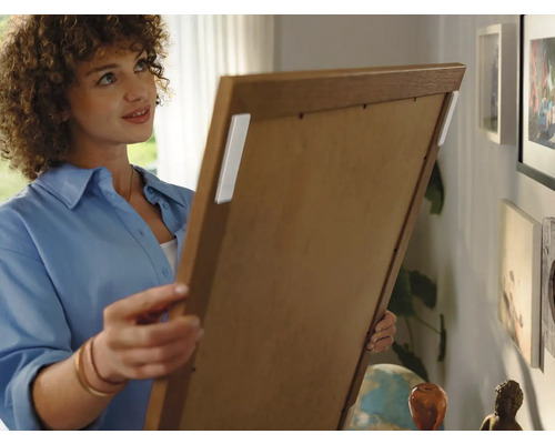 Frau befestigt ein Bild mit Klebestreifen an der Wand