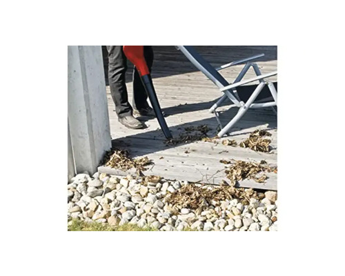 Eine Person benutzt einen Laubsauger auf einer Terrasse, umgeben von Steinen.