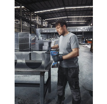 Mann montiert Metallbauteile mit Akku-Schlagschrauber in einer Werkshalle