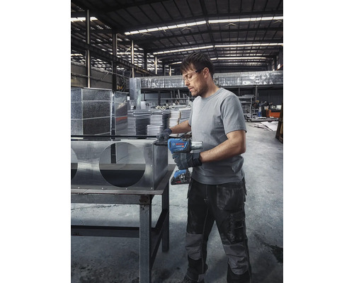 Mann montiert Metallbauteile mit Akku-Schlagschrauber in einer Werkshalle