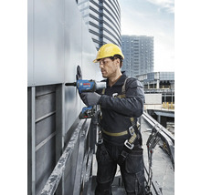 Ein Mann mit Schutzhelm und Sicherheitsgurt bedient einen Nietapparat auf einer Baustelle.