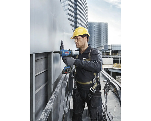 Ein Mann mit Schutzhelm und Sicherheitsgurt bedient einen Nietapparat auf einer Baustelle.