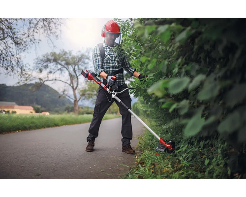 Person schneidet Hecke mit Akku-Rasentrimmer und Schutzkleidung