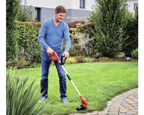 Ein Mann benutzt einen Rasentrimmer in einem Garten mit Rasenfläche.